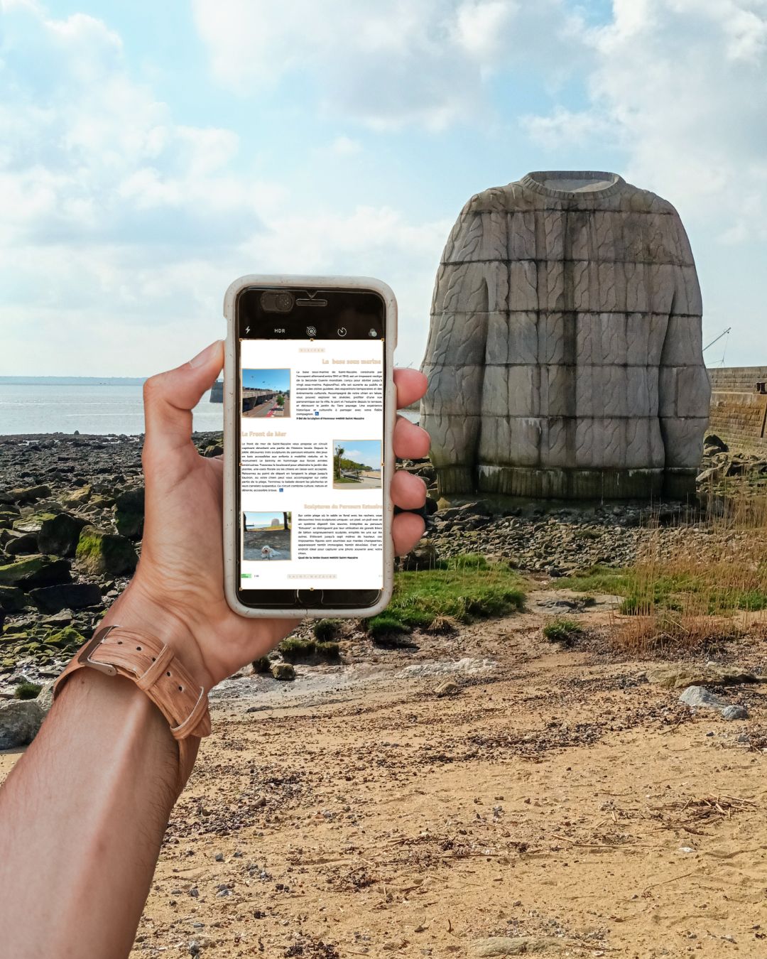 Presqu'île Guérandaise avec son chien : guide complet pour vos vacances dog-friendly : main tenant un smartphone affichant le guide PDF, en fond la vue du lieu associé (sculpture pull à Saint-Nazaire), prêt à télécharger.